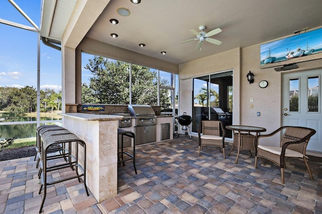 view of patio featuring area for grilling, an outdoor bar, ceiling fan, and a water view