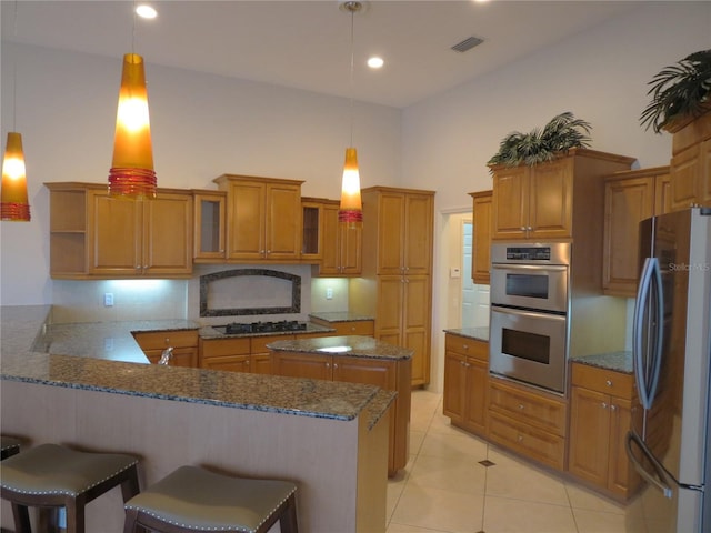 kitchen with a breakfast bar area, hanging light fixtures, stainless steel appliances, light tile patterned flooring, and kitchen peninsula