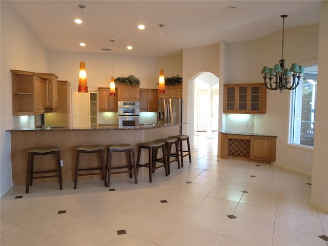 kitchen featuring light tile patterned flooring, appliances with stainless steel finishes, a breakfast bar area, dark stone counters, and kitchen peninsula