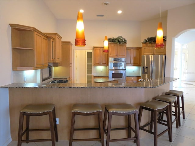 kitchen featuring light tile patterned flooring, dark stone countertops, decorative backsplash, hanging light fixtures, and stainless steel appliances