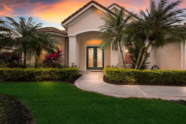 exterior entry at dusk featuring french doors and a yard