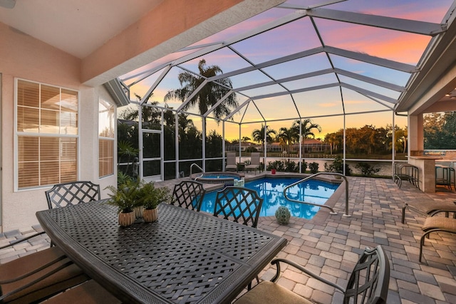 pool at dusk with a patio area, an in ground hot tub, glass enclosure, and exterior bar