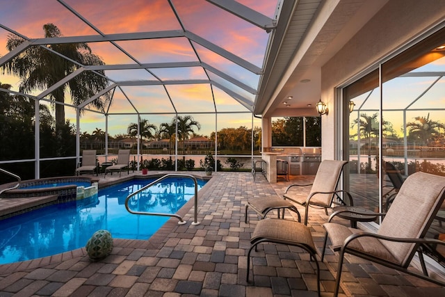 pool at dusk with area for grilling, an in ground hot tub, a patio, and glass enclosure