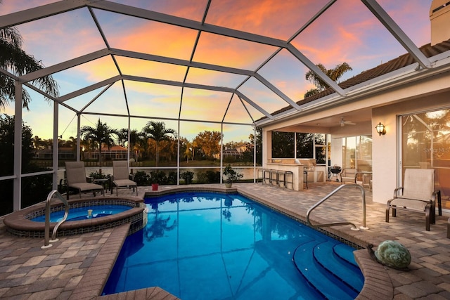 pool at dusk with a lanai, an outdoor bar, ceiling fan, a patio, and an in ground hot tub