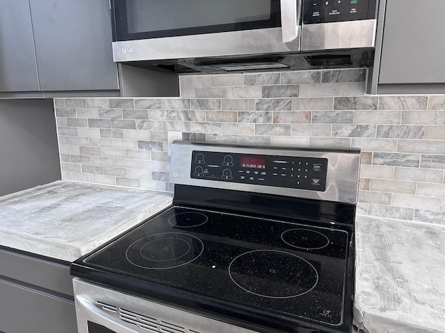 kitchen featuring gray cabinetry, stainless steel electric range oven, and decorative backsplash