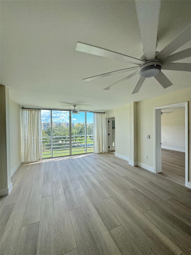 empty room with light wood-type flooring, a wall of windows, and ceiling fan