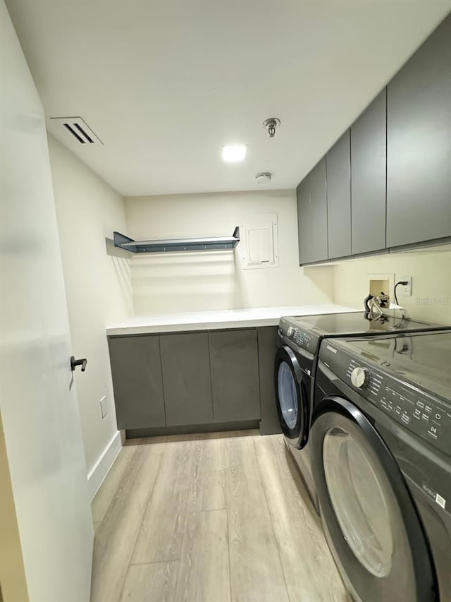 washroom featuring light wood-type flooring, washing machine and clothes dryer, and cabinets