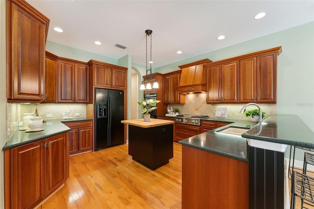 kitchen with light wood-type flooring, backsplash, black fridge with ice dispenser, and pendant lighting