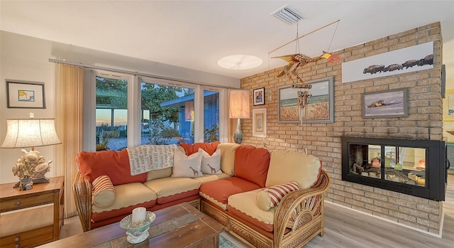 living room featuring a brick fireplace, brick wall, and light wood-type flooring