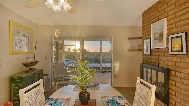 dining area featuring dark wood-type flooring, ceiling fan, and a brick fireplace