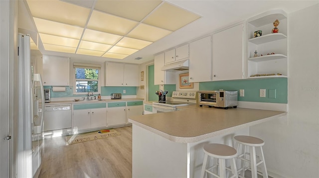 kitchen with kitchen peninsula, white appliances, white cabinets, and sink