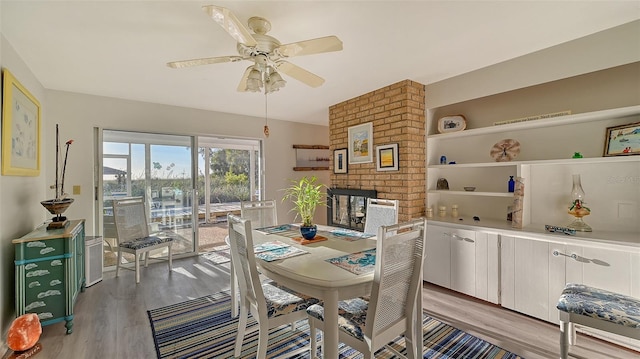 dining space featuring brick wall, light hardwood / wood-style floors, ceiling fan, and a brick fireplace