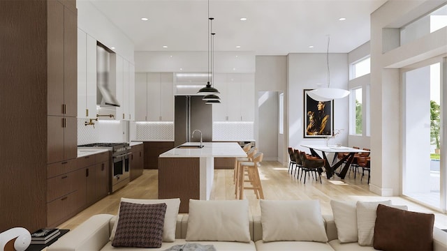 kitchen featuring an island with sink, backsplash, dark brown cabinets, range with two ovens, and pendant lighting