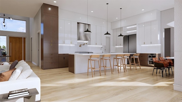 kitchen with white cabinetry, wall chimney exhaust hood, a towering ceiling, decorative backsplash, and hanging light fixtures