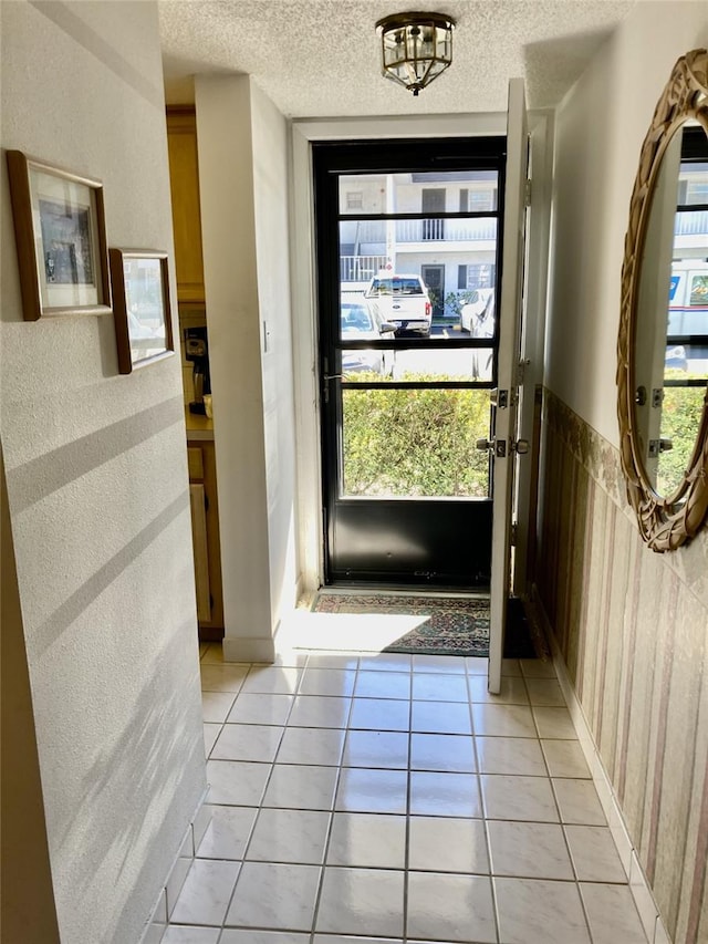 doorway to outside with light tile floors, a textured ceiling, and a wealth of natural light