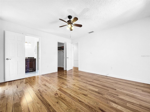 unfurnished bedroom featuring ceiling fan, a walk in closet, light hardwood / wood-style floors, ensuite bath, and a textured ceiling