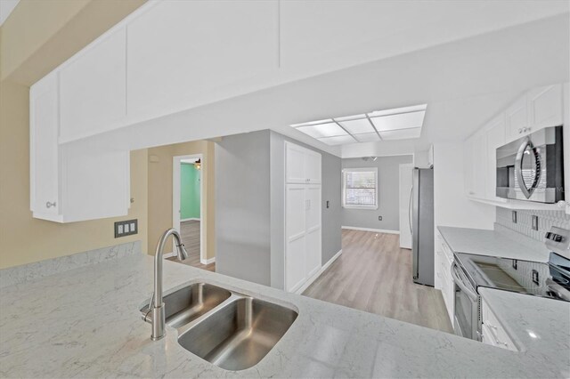 kitchen featuring white cabinets, appliances with stainless steel finishes, light stone counters, and light wood-type flooring