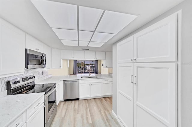 kitchen with tasteful backsplash, appliances with stainless steel finishes, white cabinetry, light wood-type flooring, and sink