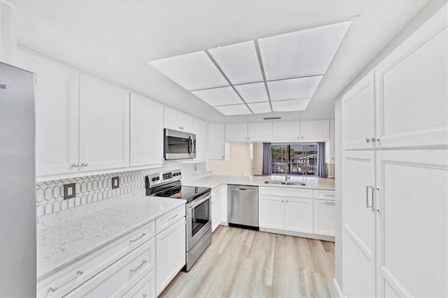 kitchen featuring appliances with stainless steel finishes, sink, light hardwood / wood-style flooring, white cabinets, and tasteful backsplash