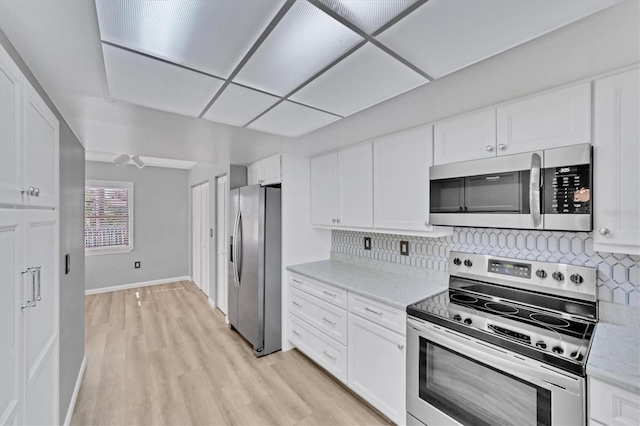 kitchen featuring tasteful backsplash, appliances with stainless steel finishes, white cabinetry, light wood-type flooring, and light stone counters