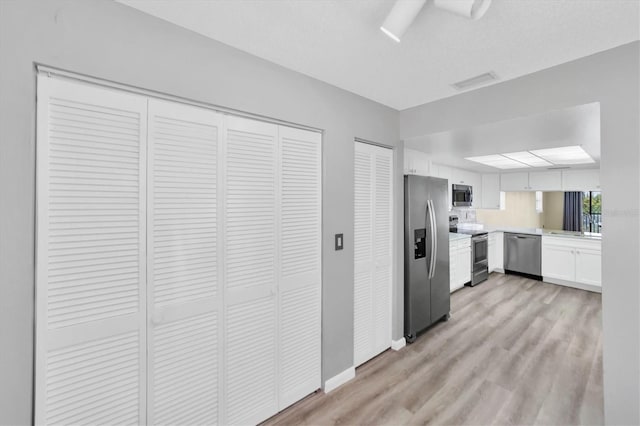 kitchen featuring white cabinets, ceiling fan, light wood-type flooring, and stainless steel appliances