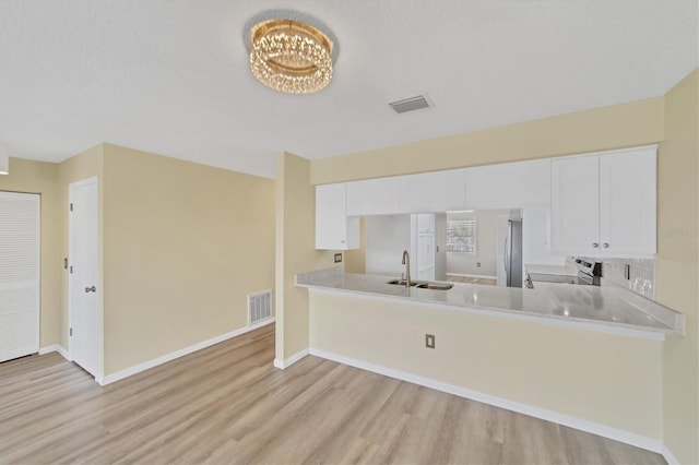 kitchen featuring kitchen peninsula, light hardwood / wood-style floors, white cabinetry, and a chandelier