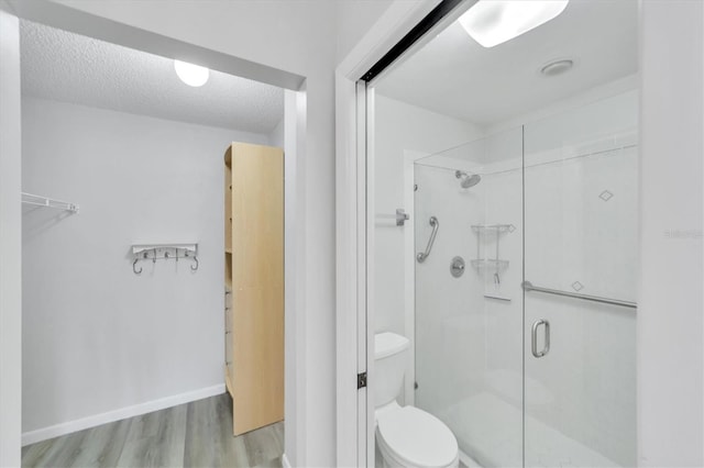 bathroom with hardwood / wood-style flooring, a shower with door, a textured ceiling, and toilet