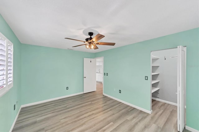 unfurnished bedroom with a closet, a spacious closet, light hardwood / wood-style floors, and ceiling fan