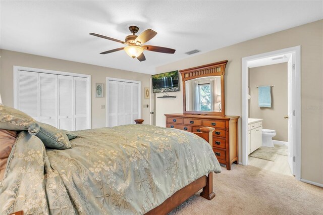 carpeted bedroom featuring two closets, ensuite bath, and ceiling fan