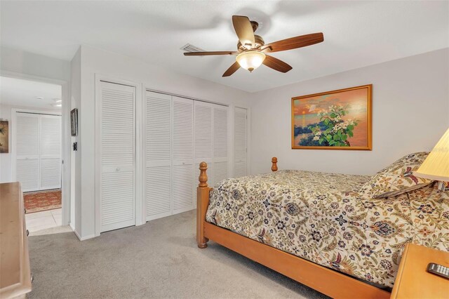 bedroom with ceiling fan, light colored carpet, and multiple closets