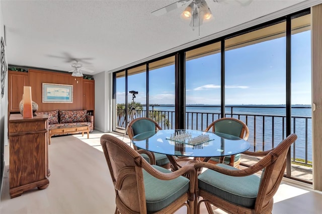 dining area featuring a textured ceiling, ceiling fan, floor to ceiling windows, and a water view