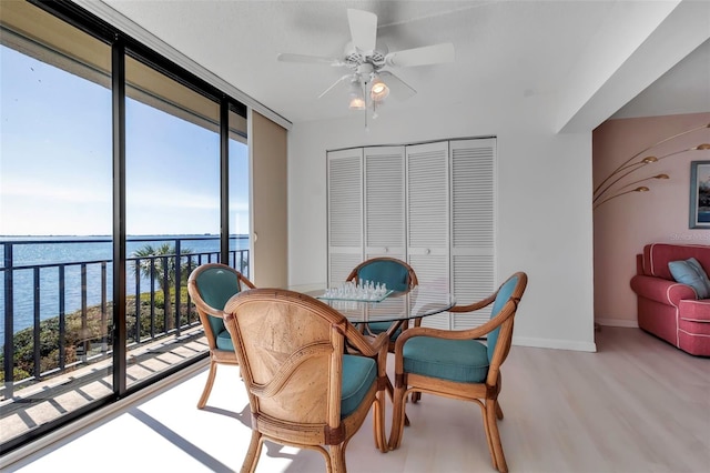 dining room with a water view, light hardwood / wood-style floors, ceiling fan, and a wall of windows