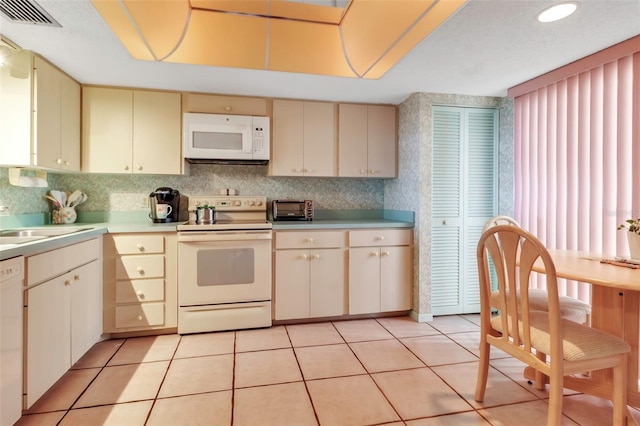 kitchen featuring light tile flooring, tasteful backsplash, white appliances, and cream cabinets