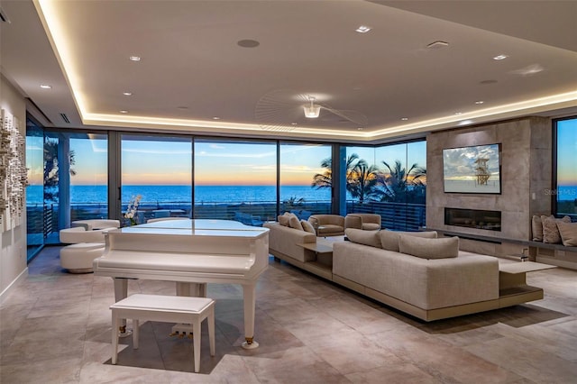 living room featuring a fireplace, floor to ceiling windows, a water view, and a tray ceiling