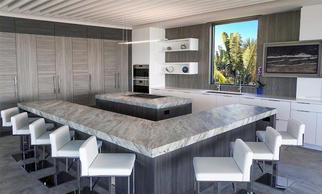 kitchen with wood walls, a center island, white cabinets, a breakfast bar, and sink