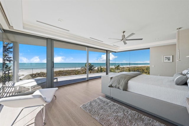 bedroom featuring ceiling fan, a wall of windows, access to outside, a view of the beach, and a water view