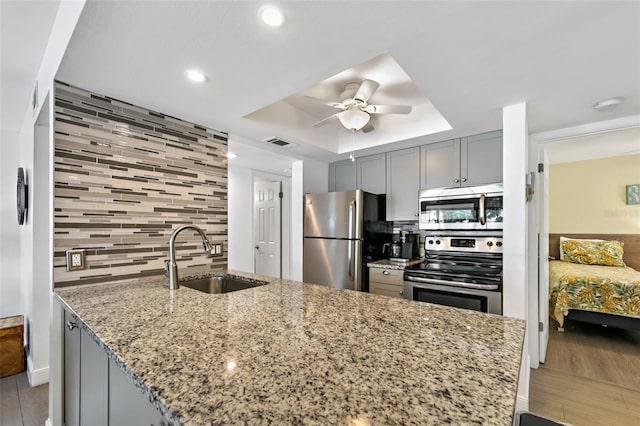 kitchen featuring stainless steel appliances, sink, backsplash, a tray ceiling, and light stone counters