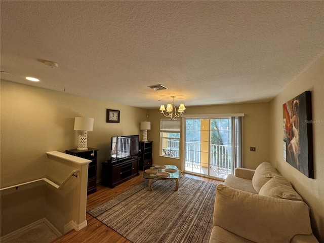 living area featuring visible vents, an inviting chandelier, a textured ceiling, wood finished floors, and baseboards