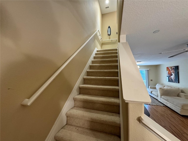 stairs featuring a textured ceiling, a ceiling fan, and baseboards