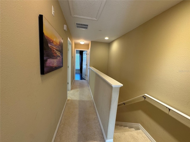 corridor featuring baseboards, visible vents, a textured wall, an upstairs landing, and carpet floors