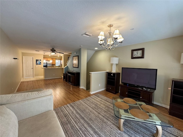 living room with ceiling fan with notable chandelier, wood finished floors, visible vents, and baseboards