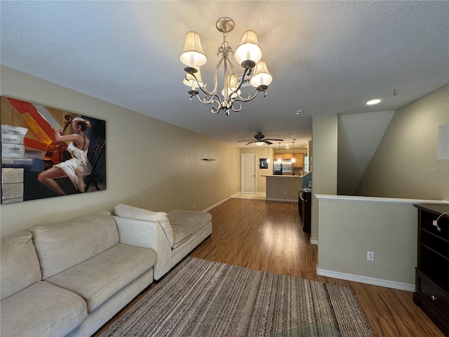 living area featuring ceiling fan with notable chandelier, a textured ceiling, baseboards, and wood finished floors