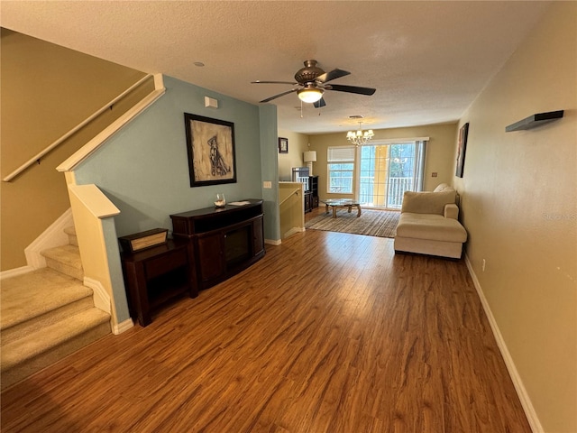 unfurnished living room featuring baseboards, stairway, wood finished floors, a textured ceiling, and ceiling fan with notable chandelier