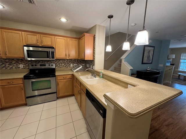 kitchen featuring a sink, light countertops, backsplash, a peninsula, and appliances with stainless steel finishes