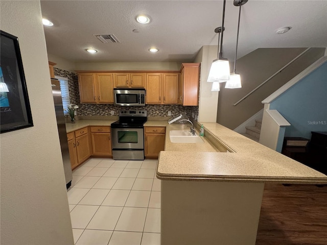 kitchen with a peninsula, a sink, stainless steel appliances, and light countertops