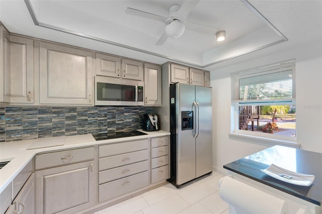 kitchen with ceiling fan, backsplash, stainless steel appliances, light tile flooring, and a tray ceiling