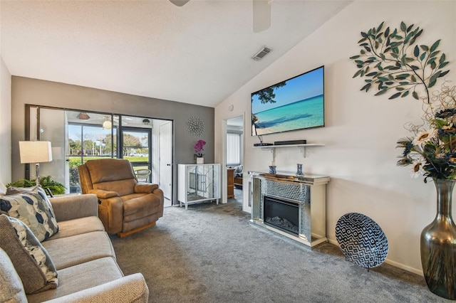 carpeted living room with ceiling fan, a tiled fireplace, and lofted ceiling