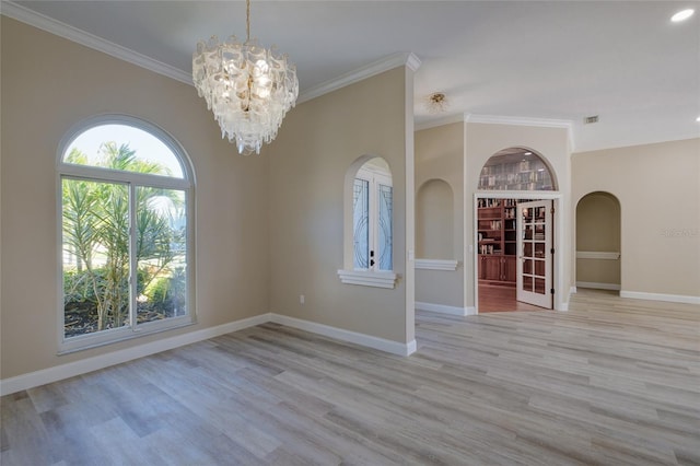 unfurnished room featuring an inviting chandelier, ornamental molding, a healthy amount of sunlight, and light wood-type flooring