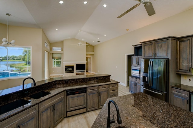 kitchen with ceiling fan with notable chandelier, light hardwood / wood-style flooring, appliances with stainless steel finishes, lofted ceiling, and dark stone countertops