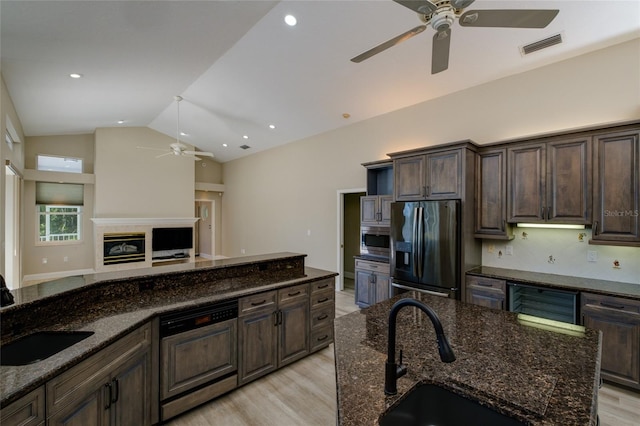 kitchen featuring ceiling fan, appliances with stainless steel finishes, light hardwood / wood-style flooring, dark stone counters, and a center island with sink